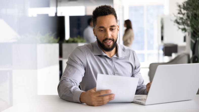 Man reviewing a document while working on a laptop in an office
