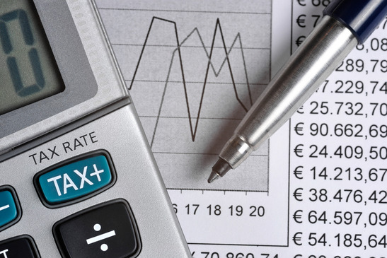 Detail-of-calculator-focusing-the-TAX-key-next-to-a-sheet-of paper-with-numbers-and-a-metal-pen