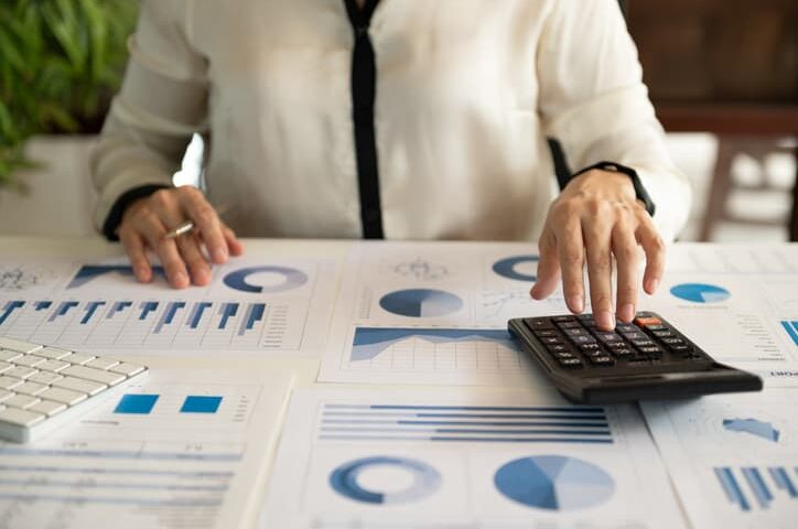 Person using a calculator while reviewing financial charts and reports on a desk