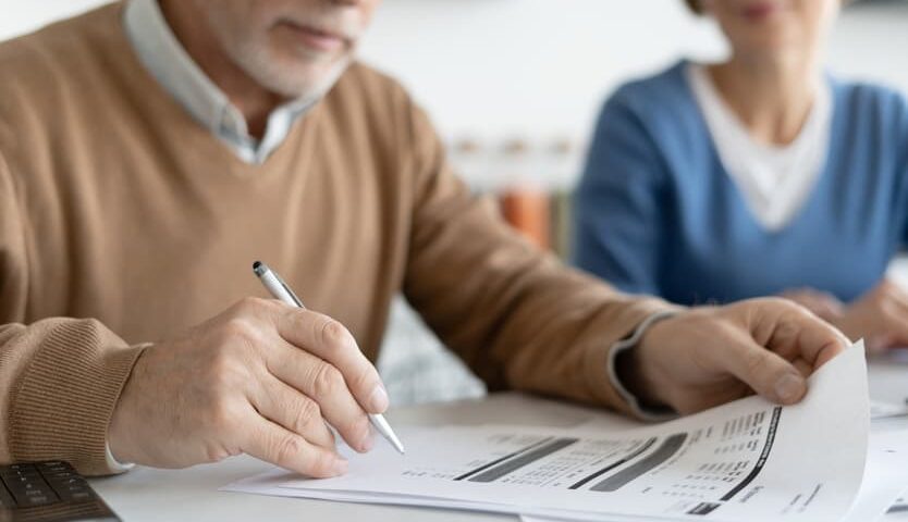 Man reviewing financial documents with a calculator while another person looks on