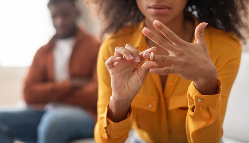 Woman removing her wedding ring while sitting apart from her partner