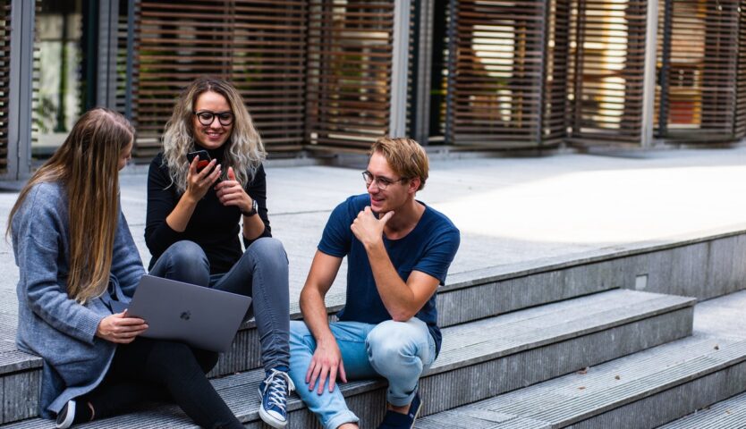 Three students sitting on concrete stairs with laptop