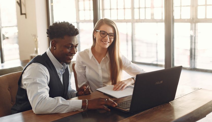 Man and woman in business attire sit in front of laptop computer