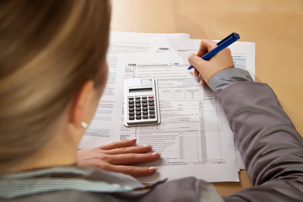 woman fills out tax form using pen and calculator