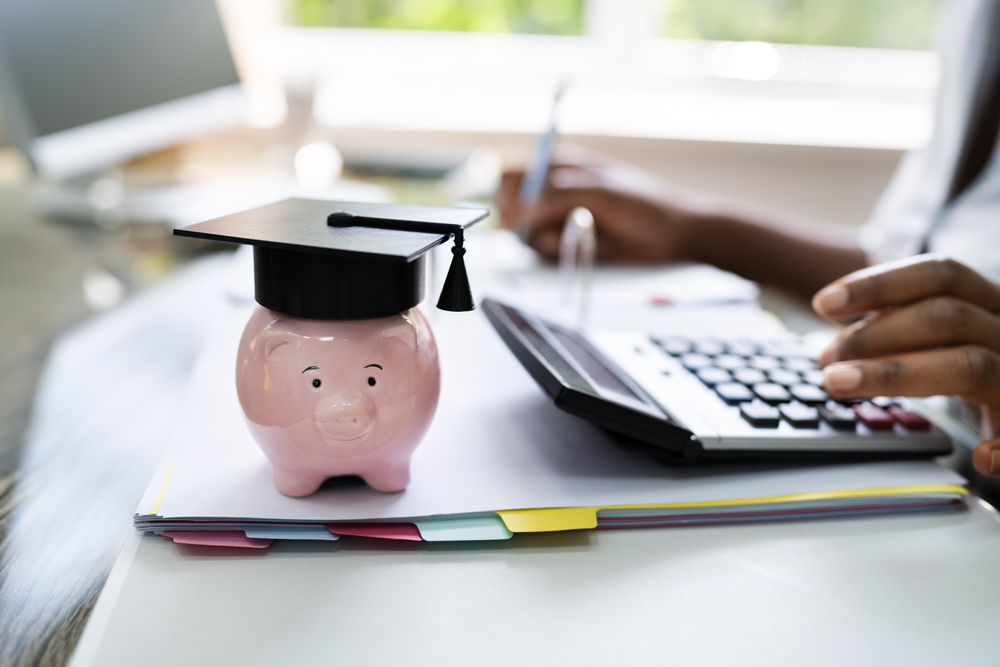 woman using calculator to do taxes beside piggy bank with graduating cap