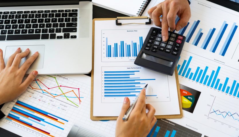 Top view of Finance business people or accountants point to the graph and use a calculator to calculate company income, expenses, taxes, and employee bonuses