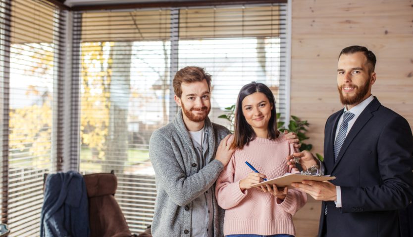 couple of tenants shaking hands with landlord, receive house key, making rent deal