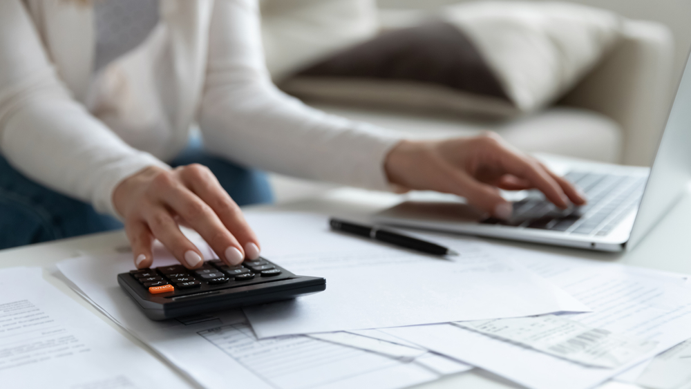 close up of woman calculating rental income taxes on laptop and calculator