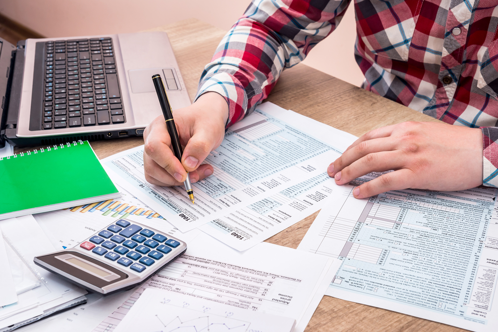 man filling tax form with help laptop caluclator and note at office desk