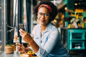 woman reading text messages on a cellphone while sitting alone at a counter in a cafe enjoying a meal