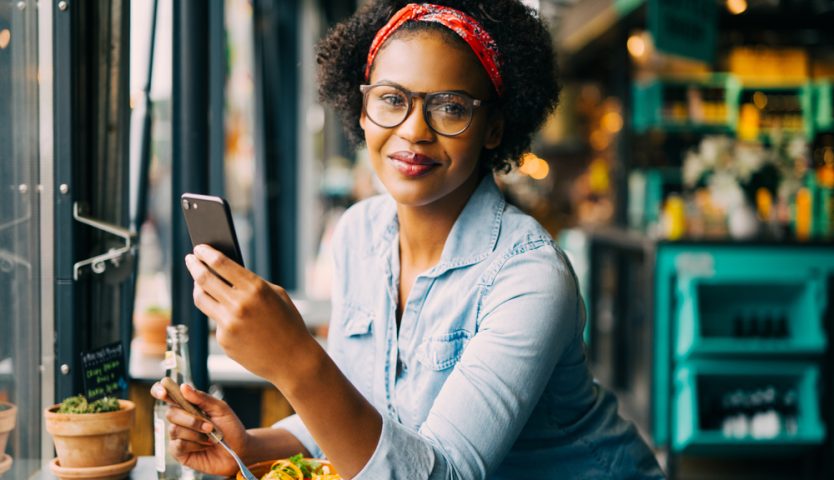 woman reading text messages on a cellphone while sitting alone at a counter in a cafe enjoying a meal