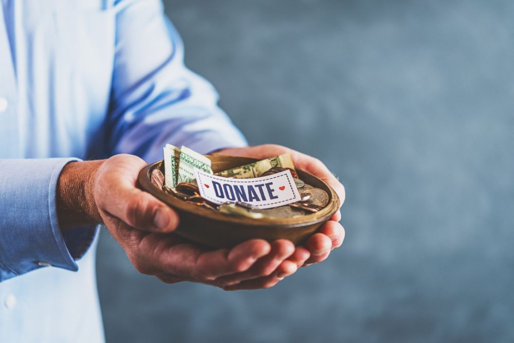 Male hands holding donation bowl with sign reading, Donate